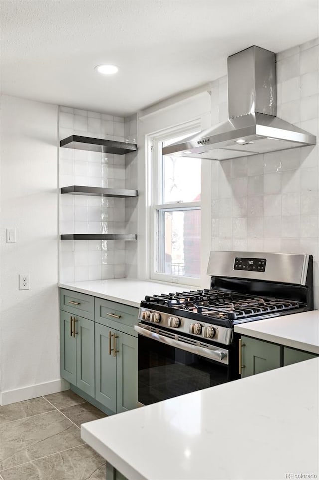 kitchen featuring stainless steel gas range, wall chimney exhaust hood, green cabinetry, and decorative backsplash