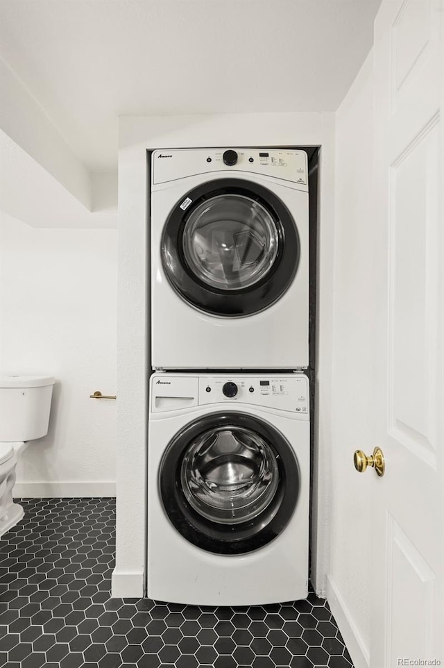 clothes washing area with dark tile patterned flooring and stacked washer and clothes dryer