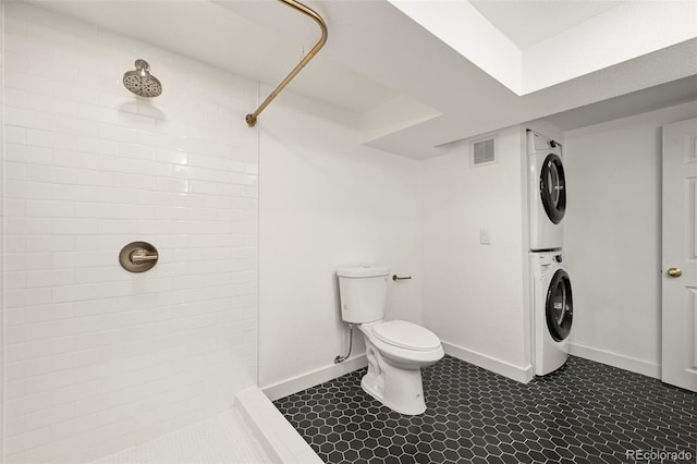 bathroom with stacked washer / drying machine, a tile shower, and toilet