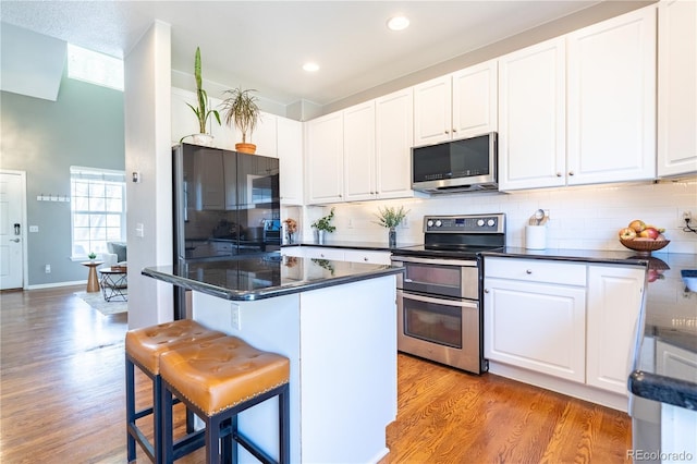 kitchen with dark countertops, light wood-type flooring, stainless steel appliances, and a kitchen bar