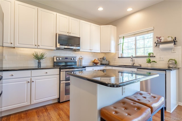 kitchen featuring stainless steel appliances, dark countertops, white cabinetry, and a sink