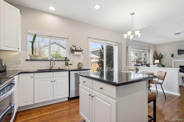 kitchen featuring wood finished floors, dark countertops, open floor plan, a sink, and stainless steel appliances