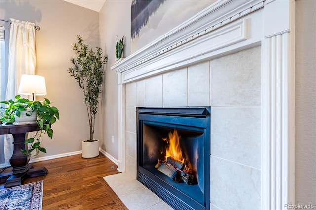 interior details featuring a tiled fireplace, baseboards, and wood finished floors