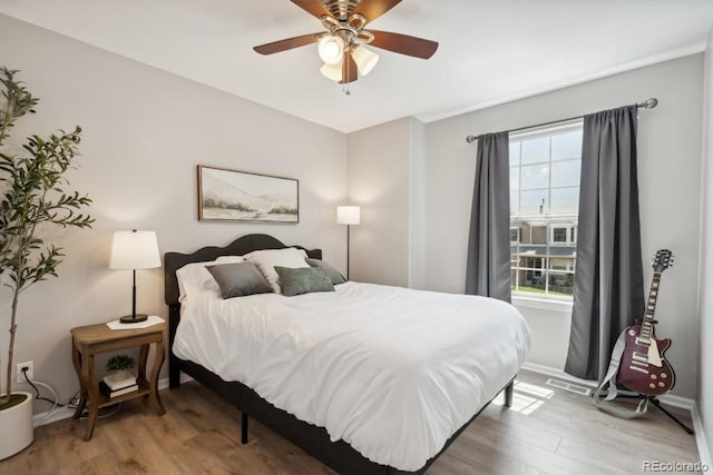 bedroom with baseboards, a ceiling fan, wood finished floors, and visible vents