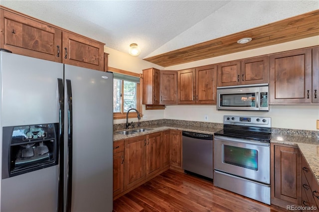 kitchen featuring stainless steel appliances, a sink, vaulted ceiling, dark wood-style flooring, and light stone countertops