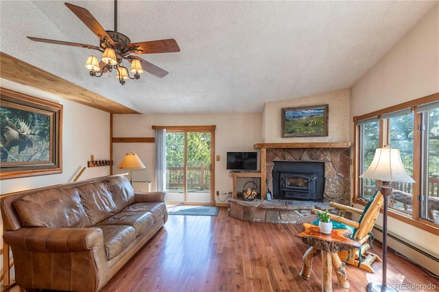 living area with a baseboard radiator, ceiling fan, a textured ceiling, hardwood / wood-style floors, and a wood stove