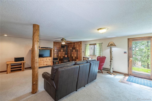 carpeted living area with a wood stove, plenty of natural light, a textured ceiling, a ceiling fan, and baseboards