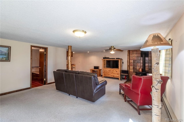 carpeted living area featuring a wood stove, a textured ceiling, a baseboard radiator, ceiling fan, and baseboards