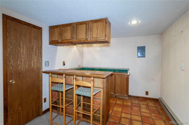 kitchen featuring a baseboard radiator, a textured ceiling, brown cabinets, baseboards, and recessed lighting