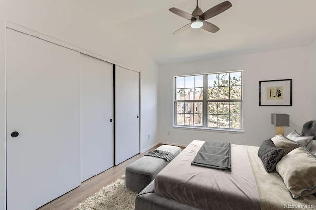 bedroom featuring a closet, lofted ceiling, baseboards, light wood-type flooring, and a ceiling fan
