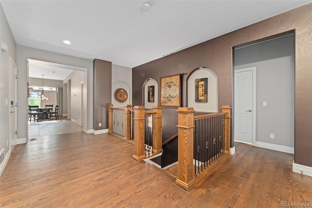 hall with an upstairs landing, wood finished floors, baseboards, recessed lighting, and arched walkways