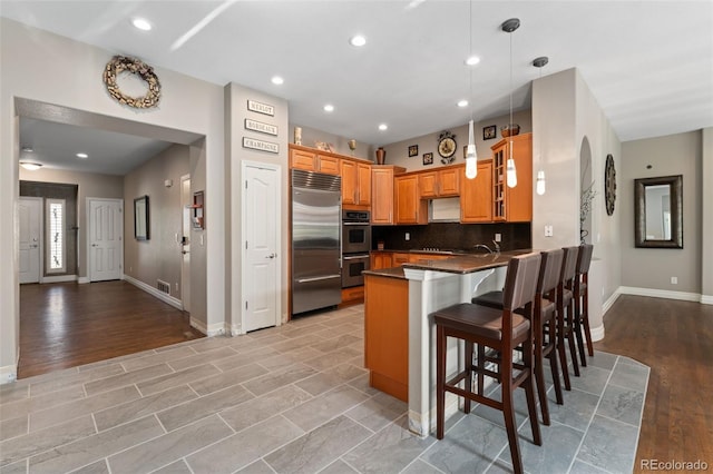 kitchen with stainless steel appliances, a peninsula, dark countertops, baseboards, and a breakfast bar