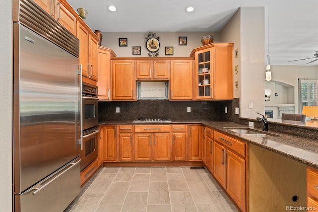kitchen featuring appliances with stainless steel finishes, a sink, dark stone countertops, glass insert cabinets, and recessed lighting