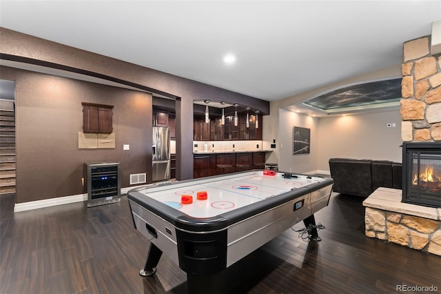 game room featuring beverage cooler, dark wood-style flooring, a stone fireplace, and baseboards