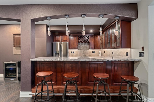 indoor wet bar featuring stainless steel refrigerator with ice dispenser, wine cooler, tasteful backsplash, dark wood finished floors, and a textured wall