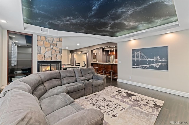 living room featuring a raised ceiling, baseboards, dark wood-style flooring, a fireplace, and arched walkways