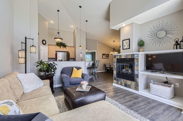 living area with high vaulted ceiling, wood finished floors, baseboards, a tile fireplace, and a chandelier