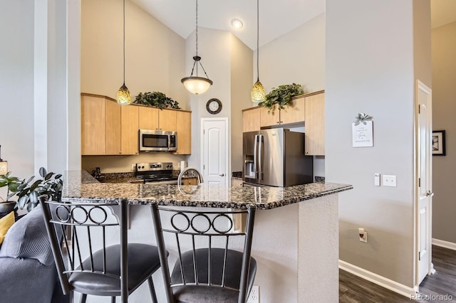 kitchen featuring stainless steel appliances, high vaulted ceiling, light brown cabinets, a peninsula, and dark stone countertops