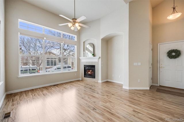 unfurnished living room with visible vents, a towering ceiling, light wood-type flooring, baseboards, and a tile fireplace