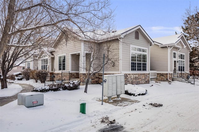 snow covered property featuring a garage, stone siding, and mail area