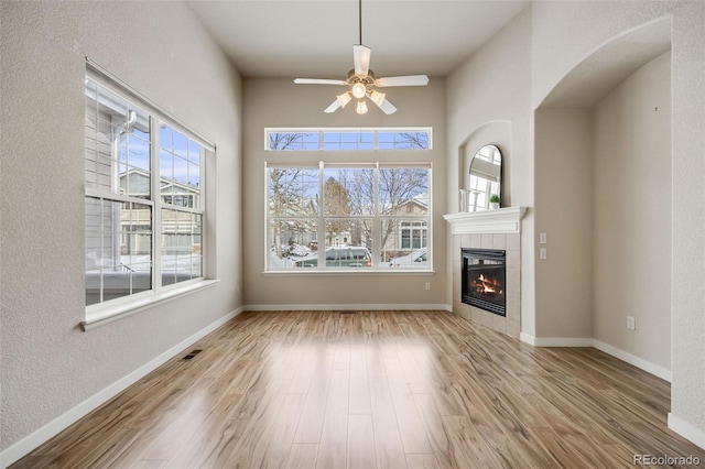 unfurnished living room with a ceiling fan, a fireplace, baseboards, and wood finished floors