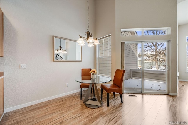 dining area featuring wood finished floors, visible vents, a towering ceiling, baseboards, and an inviting chandelier