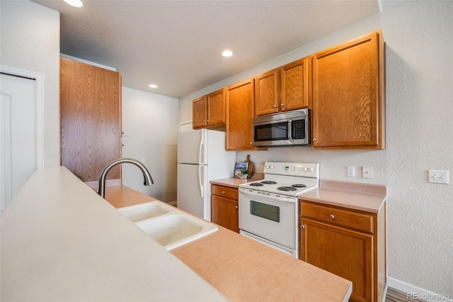 kitchen with brown cabinets, white appliances, light countertops, and a sink