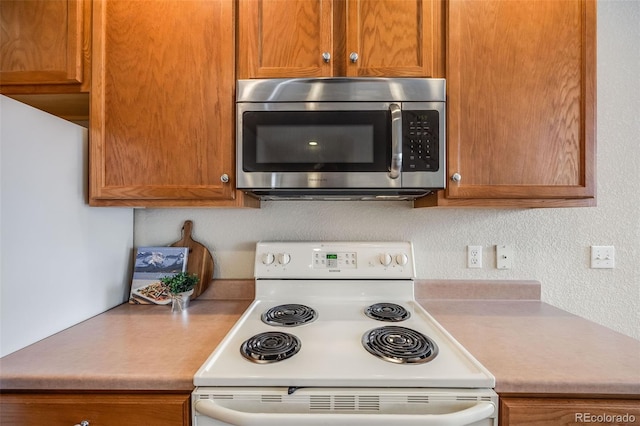 kitchen with brown cabinets, light countertops, stainless steel microwave, and white electric range oven