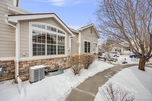 snow covered property featuring stone siding and central AC unit