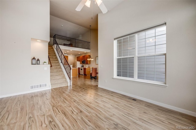 unfurnished living room with visible vents, wood finished floors, high vaulted ceiling, baseboards, and stairs