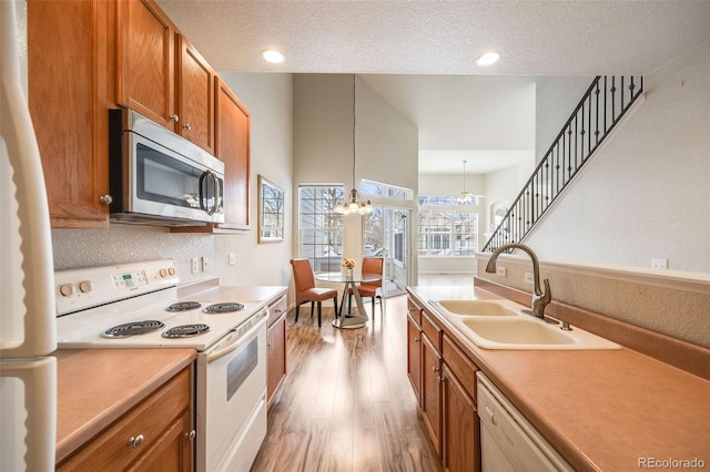 kitchen featuring light wood finished floors, white appliances, brown cabinetry, an inviting chandelier, and a sink