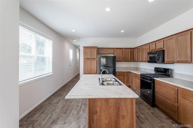 kitchen featuring black appliances, a center island with sink, hardwood / wood-style flooring, and sink