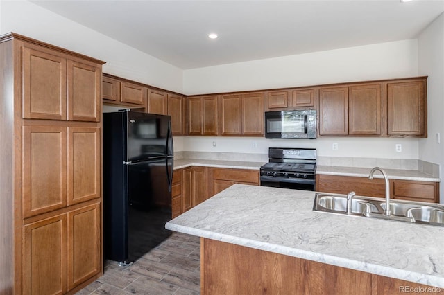 kitchen with black appliances, light stone counters, hardwood / wood-style flooring, and sink