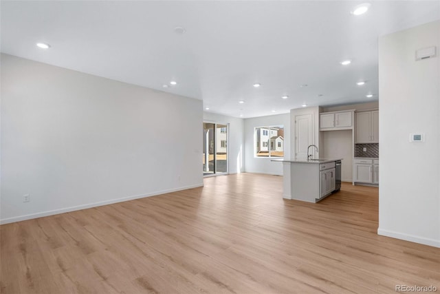 unfurnished living room with a sink, recessed lighting, light wood-type flooring, and baseboards