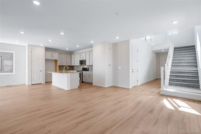unfurnished living room with a sink, light wood-type flooring, baseboards, stairway, and recessed lighting