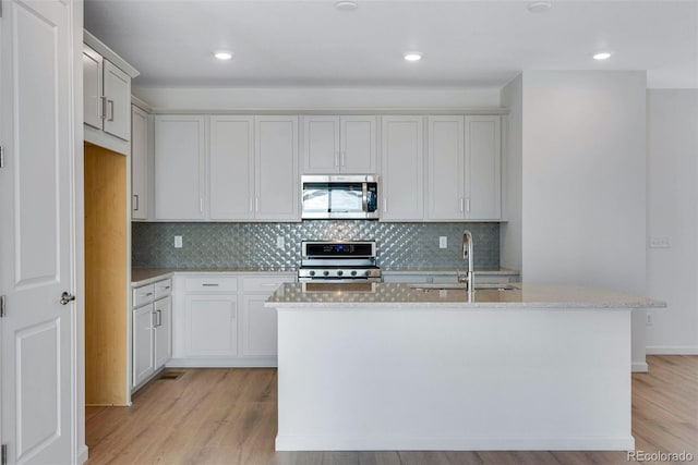 kitchen with appliances with stainless steel finishes, a sink, light wood-style flooring, a kitchen island with sink, and recessed lighting