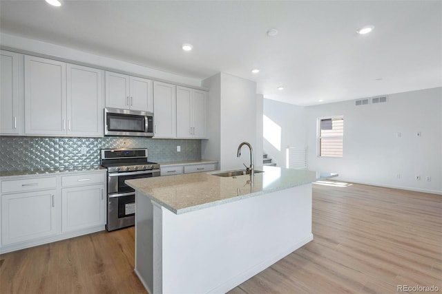 kitchen featuring appliances with stainless steel finishes, a sink, light wood-style flooring, light stone countertops, and decorative backsplash