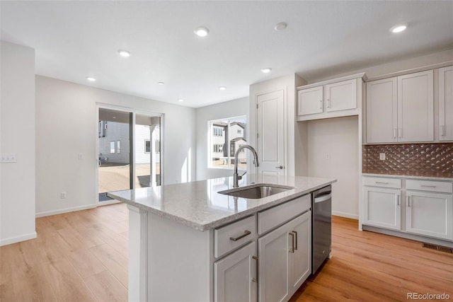 kitchen featuring a center island with sink, sink, tasteful backsplash, light stone countertops, and light wood-type flooring