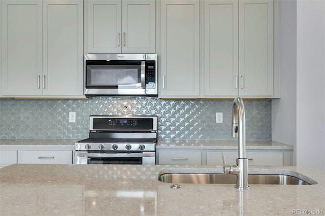 kitchen with tasteful backsplash, appliances with stainless steel finishes, sink, and light stone counters