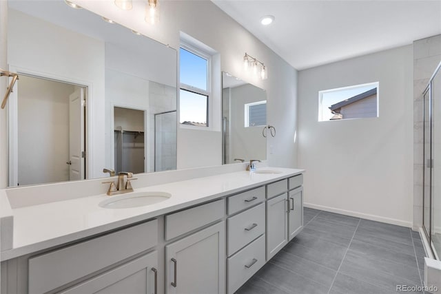 bathroom featuring double vanity, tiled shower, baseboards, a spacious closet, and tile patterned floors