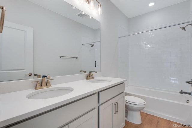 bathroom with toilet, wood finished floors, double vanity, and washtub / shower combination