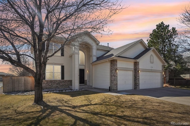 traditional-style home featuring fence, an attached garage, a yard, concrete driveway, and stone siding