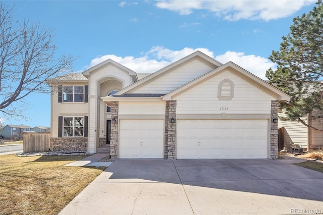 traditional-style house featuring a front lawn, driveway, stone siding, fence, and a garage