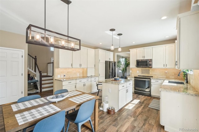 kitchen with wood finished floors, a kitchen island, a sink, appliances with stainless steel finishes, and white cabinetry