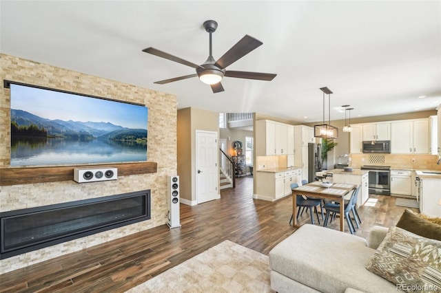 living area with wood finished floors, a stone fireplace, baseboards, ceiling fan, and stairs