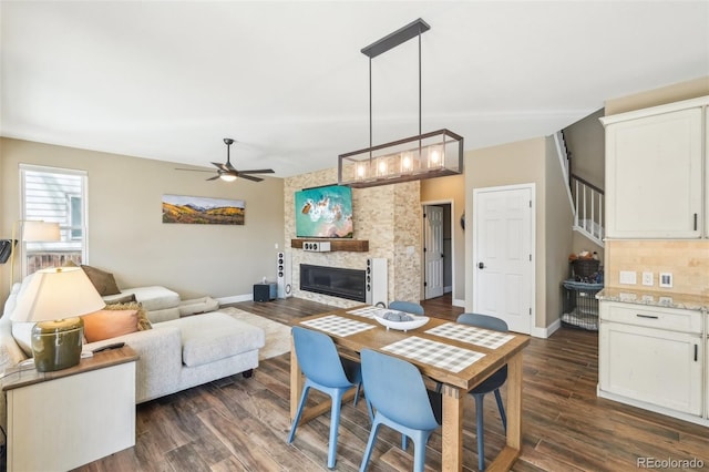 living area featuring a large fireplace, ceiling fan, baseboards, dark wood-type flooring, and stairway