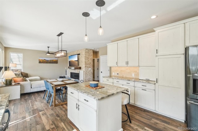 kitchen featuring dark wood-type flooring, open floor plan, hanging light fixtures, stainless steel fridge, and white cabinetry