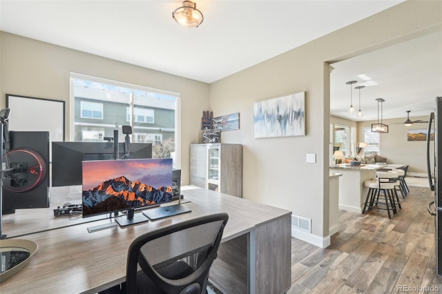 office area with a wealth of natural light, visible vents, baseboards, and wood finished floors