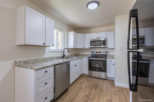 6013 W 62nd Ave, Arvada, CO 80033 - kitchen featuring appliances with stainless steel finishes, a sink, light wood-style flooring, white cabinets, and light stone counters
