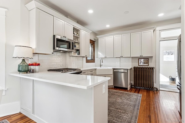 kitchen featuring radiator, sink, stainless steel appliances, white cabinets, and kitchen peninsula